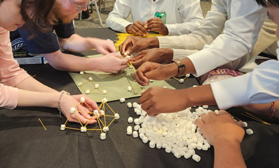 Photo: hands making bridge out of noodles and marshmallows.